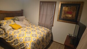 A bedroom with a bed, a window with curtains, a framed picture on the wall, and a small table with a lamp. - Spacious 4-bedroom house in tranquil Farmington with yard and fire pit. (Farmington)