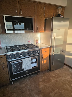 A kitchen with wooden cabinets, a stainless steel refrigerator, a gas stove, and a built-in oven. - Spacious 4-bedroom house in tranquil Farmington with yard and fire pit. (Farmington)