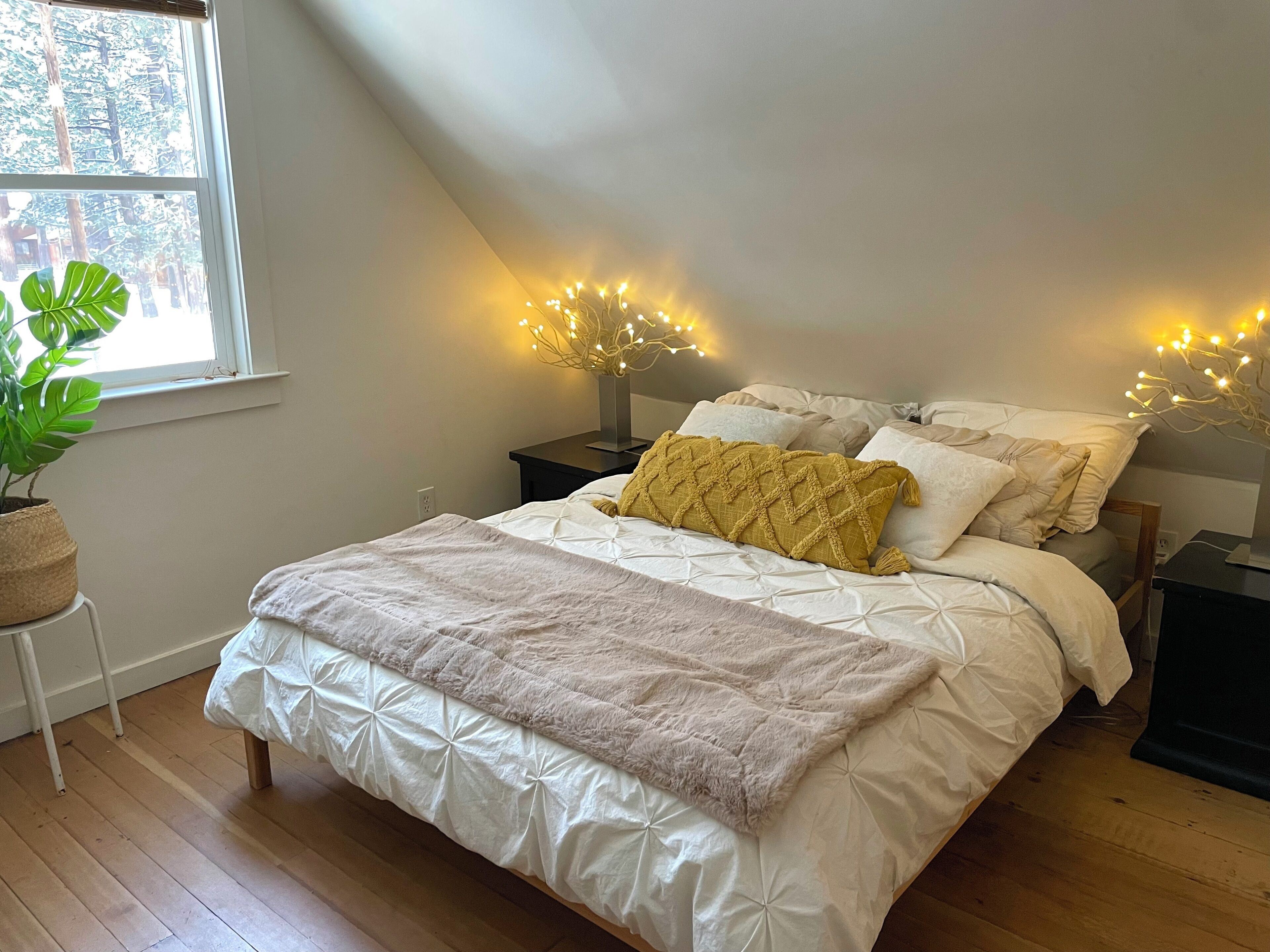 Un dormitorio con cama, mesitas de noche, una planta en maceta y luces colgantes.
