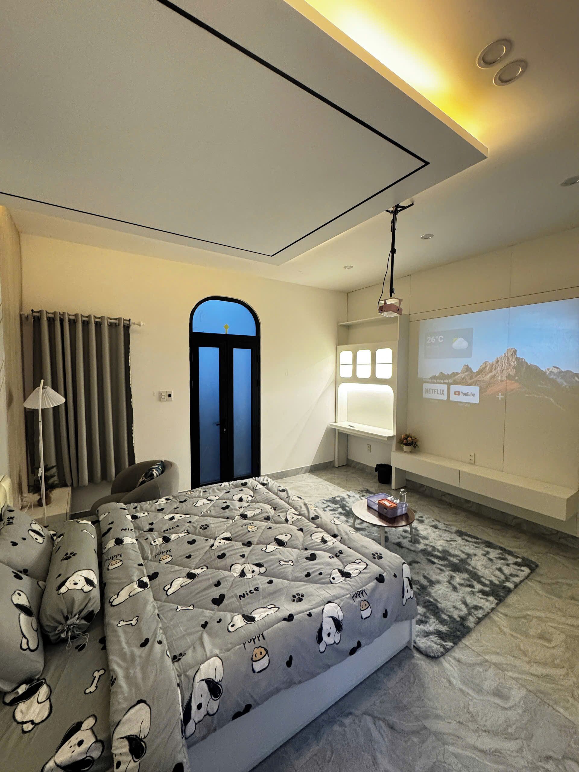 Una moderna camera d'albergo con un letto, una scrivania e un grande schermo che mostra un paesaggio montano.