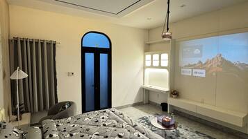 Una moderna camera d'albergo con un letto, una scrivania e un grande schermo che mostra un paesaggio montano.