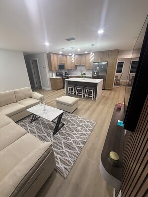 A modern kitchen with wooden cabinets, a central island, and a dining area with a sofa and coffee table. - Perfect 3-Bedroom 2-Bathroom  completely remodeled and brand new furniture (Tampa)
