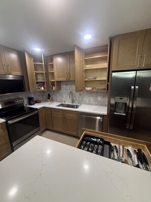 Eine moderne Küche mit Holzschränken, einem Edelstahlkühlschrank, einem eingebauten Backofen und einer Marmorarbeitsplatte.