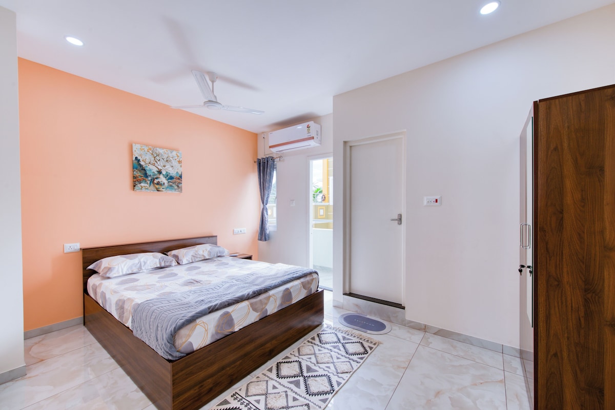 Un dormitorio con una cama, ventilador de techo, equipo de aire acondicionado, una puerta y una alfombra de baño.