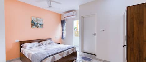 Une chambre à coucher comprenant un lit, un ventilateur de plafond, un appareil de climatisation, une porte et un tapis de bain.