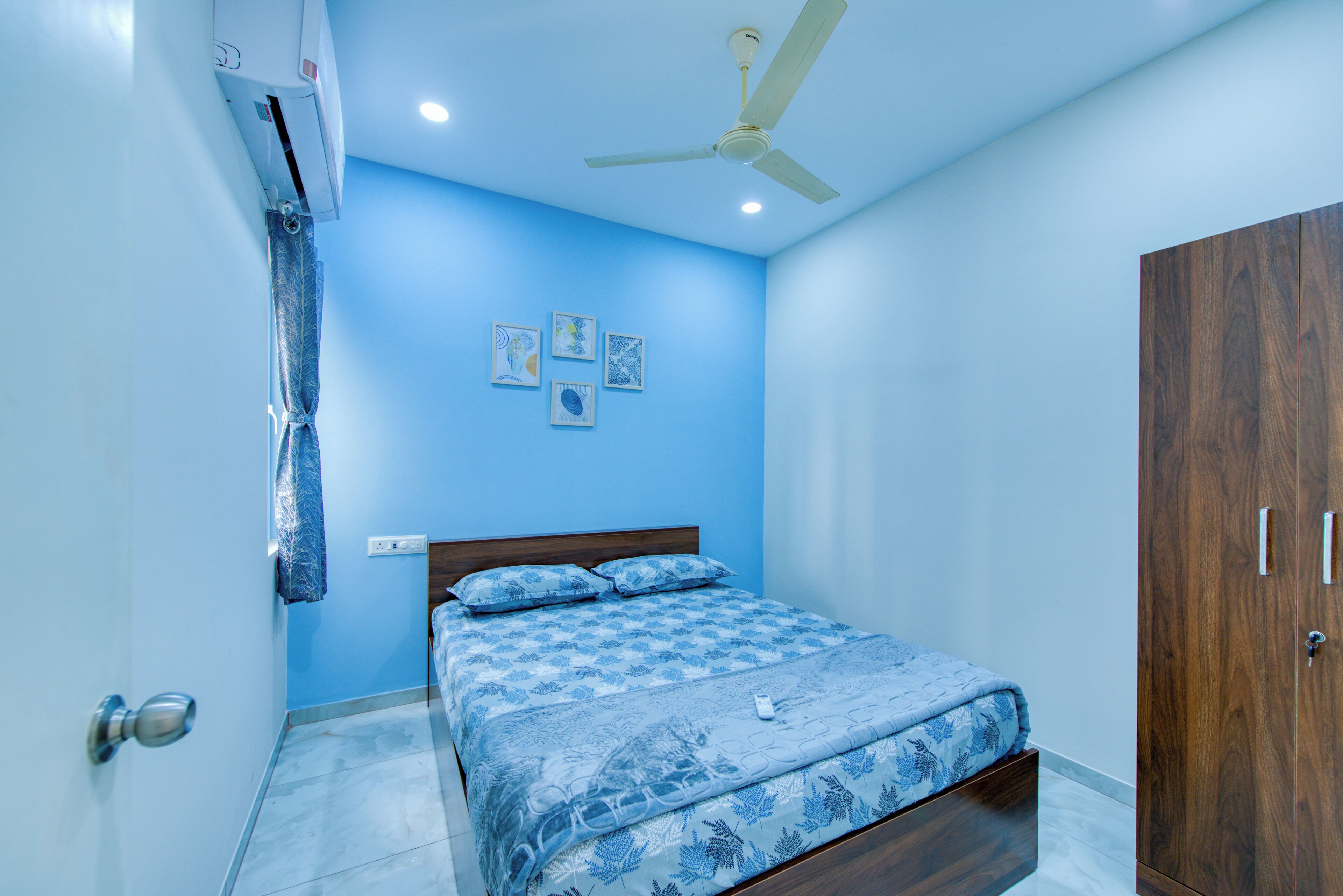 Une chambre à coucher comprenant un lit, une armoire, un ventilateur de plafond et des œuvres d’art accrochées au mur.