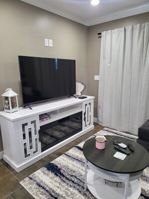 A living room with a flat-screen TV on a white entertainment unit, a coffee table with remote controls, and a patterned rug. - Tranquil 1-bedroom studio with AC in charming Chula Vista (Chula Vista)