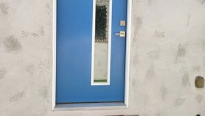 Eine blaue Tür mit weißem Rahmen, ein kleines Fenster und eine Fußmatte mit dem Wort 'WELCOME'.