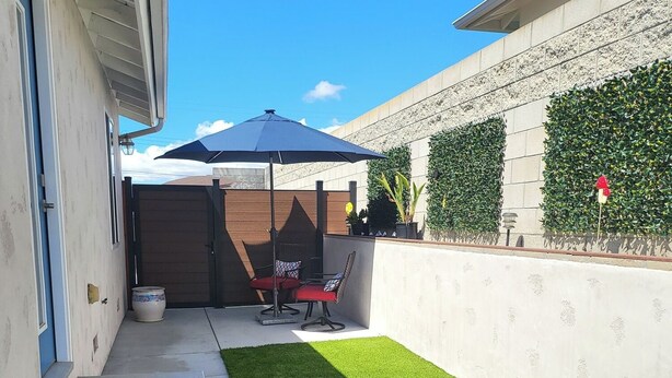 Ein wohnlicher Garten mit künstlichem Rasen, einer Terrasse mit Stühlen und einem großen Sonnenschirm.
