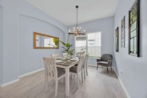 A dining area with a round table, chairs, a chandelier, and a mirror on the wall. - 5BR Disney Home, Private Pool, Spa & PS5 Game Loft (Davenport)