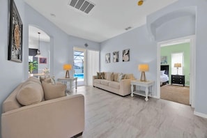 A spacious living area with a beige sofa, a white coffee table, and a beige armchair. There is a white lamp on a side table, and a painting on the wall. - 5BR Disney Home, Private Pool, Spa & PS5 Game Loft (Davenport)