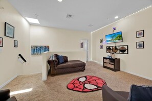 A living room with a brown sofa, a red and black rug, a television mounted on the wall, and a small cabinet. - 5BR Disney Home, Private Pool, Spa & PS5 Game Loft (Davenport)