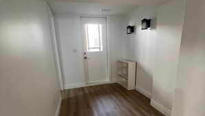 A hallway with wooden flooring, a white door with a window, and a wall-mounted light fixture. - Cozy 2-bedroom house in fantastic Windsor with AC (Windsor)
