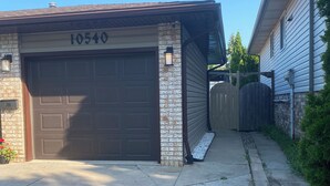 A residential garage with a number '10540' above the door, a stone facade, and a wooden fence in the background. - Cozy 2-bedroom house in fantastic Windsor with AC (Windsor)