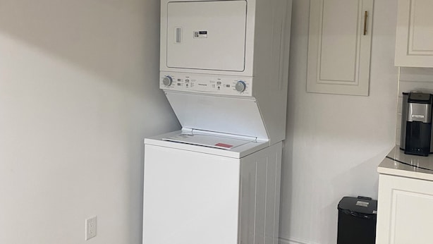 A laundry room with a stacked washer and dryer, a trash bin, and a coffee maker on a counter. - Cozy 2-bedroom house in fantastic Windsor with AC (Windsor)