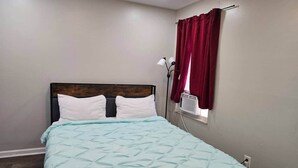 A bedroom with a bed, a nightstand, a lamp, and a window with curtains.