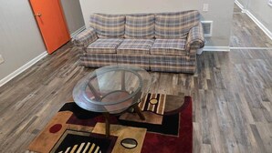 A living room with a plaid sofa, a glass coffee table, and a patterned rug.