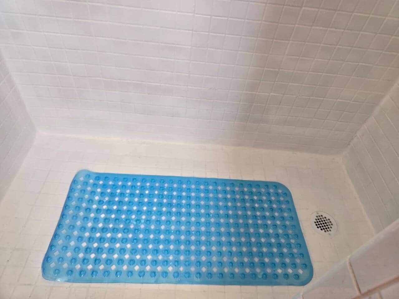 Ein Duschbereich mit blauer Fußmatte und Abfluss.