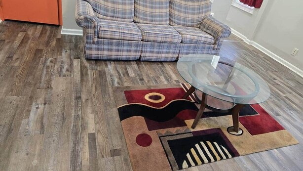A living room with a plaid sofa, a glass coffee table, and a patterned rug.