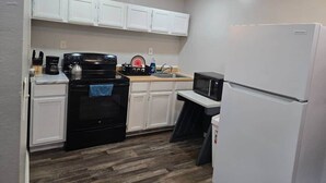 A compact kitchen with white cabinets, a black stove, a microwave, and a white refrigerator.
