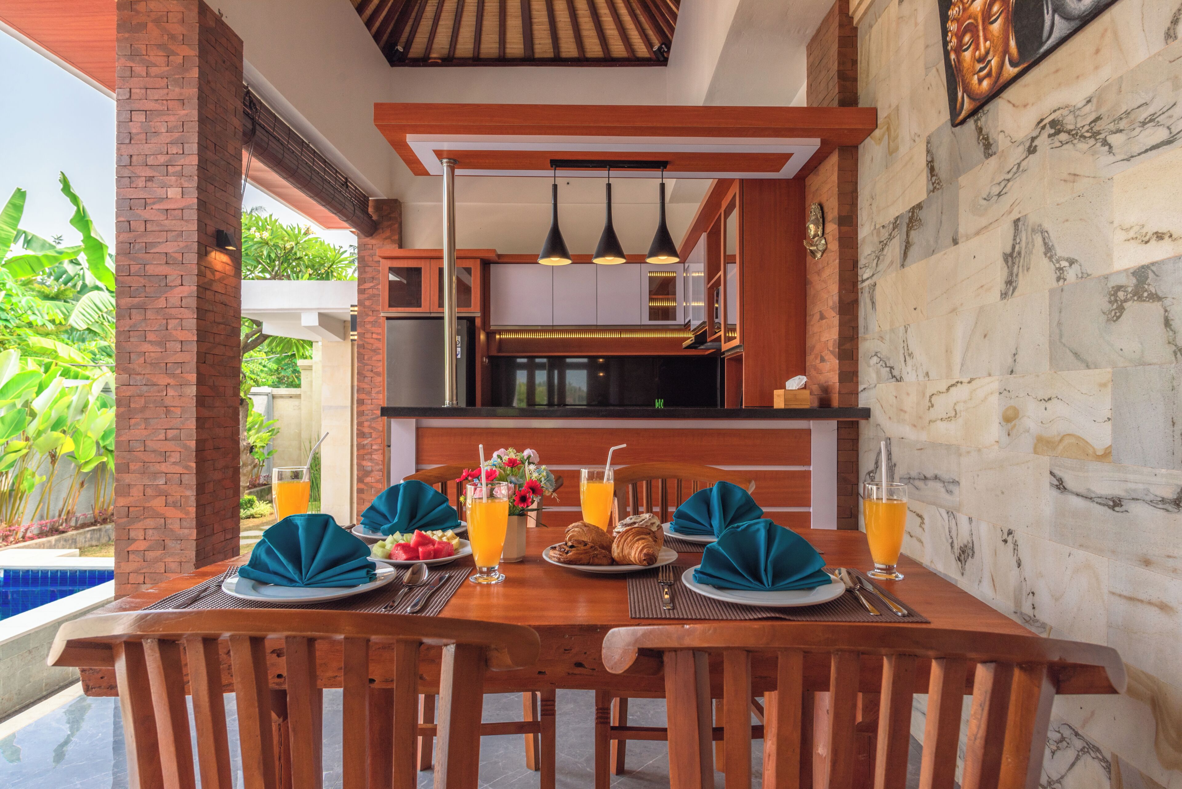 Uma área de refeições com mesa de madeira posta para dois, incluindo pratos, guardanapos e copos de suco de laranja.