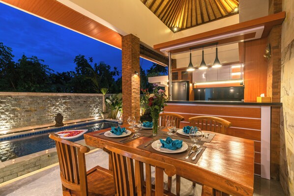 A dining area with a pool view, wooden furniture, and a modern kitchen.