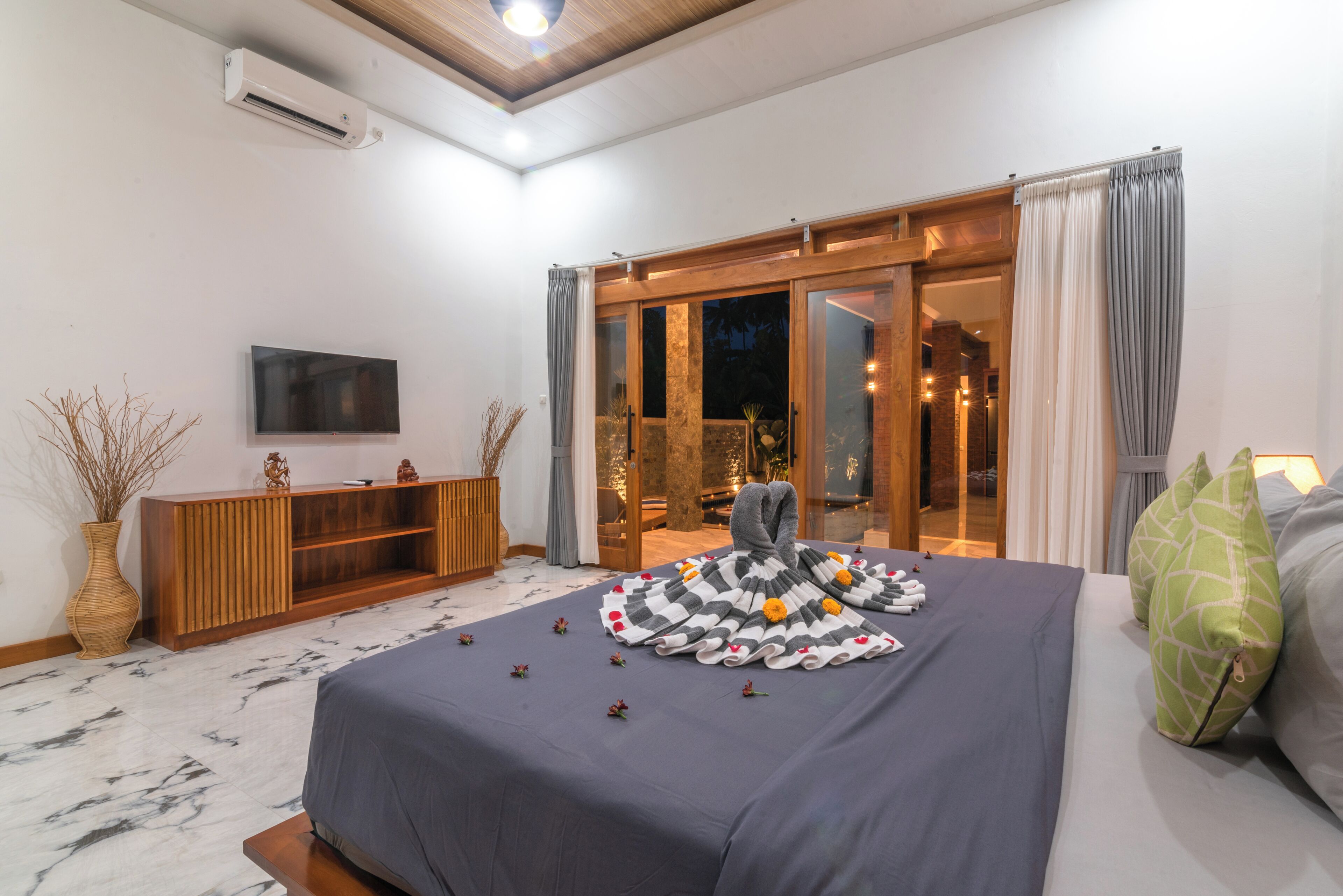 Ein Hotelzimmer mit Bett, Flachbildfernseher, einem Holzkonsolentisch und einer Glastür zum Außenbereich.
