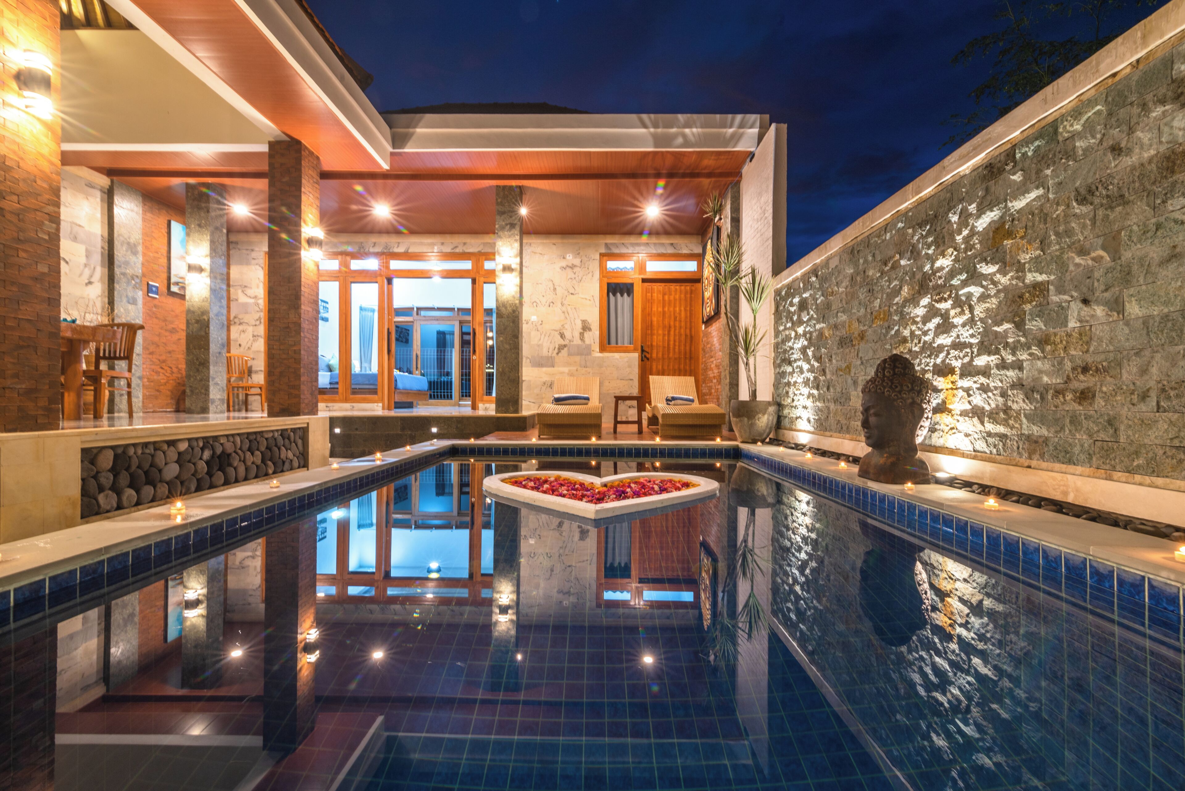 Una piscina con diseño de corazón, rodeada por un muro de piedra y una terraza de madera.