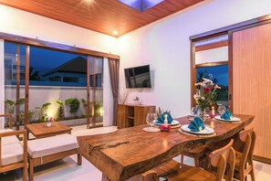 Un coin repas avec une table en bois dressée pour quatre personnes, un téléviseur fixé au mur et une vue sur l’extérieur.
