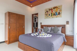 A bedroom with a large bed, wooden wardrobe, a painting on the wall, and a nightstand with a lamp. - Genta Villa, Lovina - Villa Dua (Buleleng)