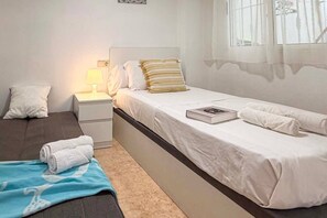 Ein Hotelzimmer mit einem Einzelbett, einem Nachttisch mit Lampe, einem kleinen Tisch und einem Fenster mit Vorhängen.