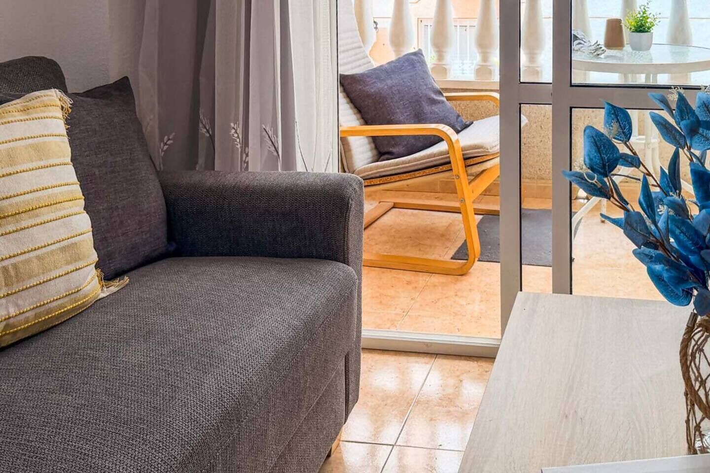 Ein modernes Wohnzimmer mit einem grauen Sofa, einem Holzstuhl und einer Glastür zum Außenbereich.