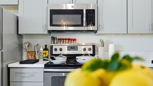 Uma cozinha moderna com eletrodomésticos de aço inoxidável, incluindo micro-ondas e fogão, e um balcão com utensílios de cozinha e uma garrafa de azeite.