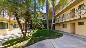 Um pátio com palmeiras, um caminho de concreto e um edifício com varandas.