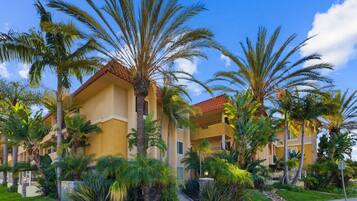 A multi-story hotel with a yellow facade and red-tiled roof, surrounded by palm trees and lush greenery.