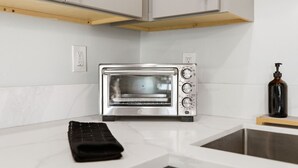 Uma cozinha com um forno elétrico de aço inoxidável, uma carteira preta no balcão e uma garrafa de sabonete.