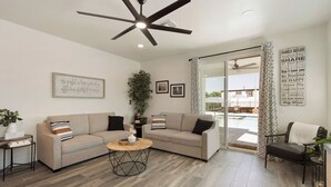 A living room with a sectional sofa, a coffee table, a ceiling fan, and a view of a pool through a glass door. - Private Resort Estate, Pool, Casita & Pavilion-12 miles from Cardinals Stadium (Peoria)