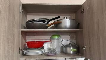 A kitchen cabinet with cookware, a colander, a glass, and a hanging rack with utensils.