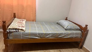 A single bed with a wooden frame, a grey bedspread with yellow lines, a leopard print blanket, and a single pillow.