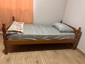 A single bed with a wooden frame, a grey bedspread with yellow lines, a leopard print blanket, and a single pillow.