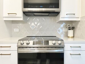 A modern kitchen with a stainless steel range and oven, white cabinetry, and a microwave above. - Chic Little Italy Condo - Pool, Valet Parking (San Diego)