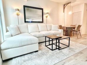 A modern living room with a sectional sofa, a coffee table, and a dining area with chairs and a table. - Chic Little Italy Condo - Pool, Valet Parking (San Diego)