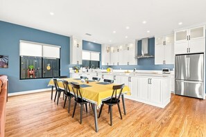 Une cuisine moderne avec des meubles blancs, un réfrigérateur en acier inoxydable et un coin repas agrémenté d’une nappe jaune.