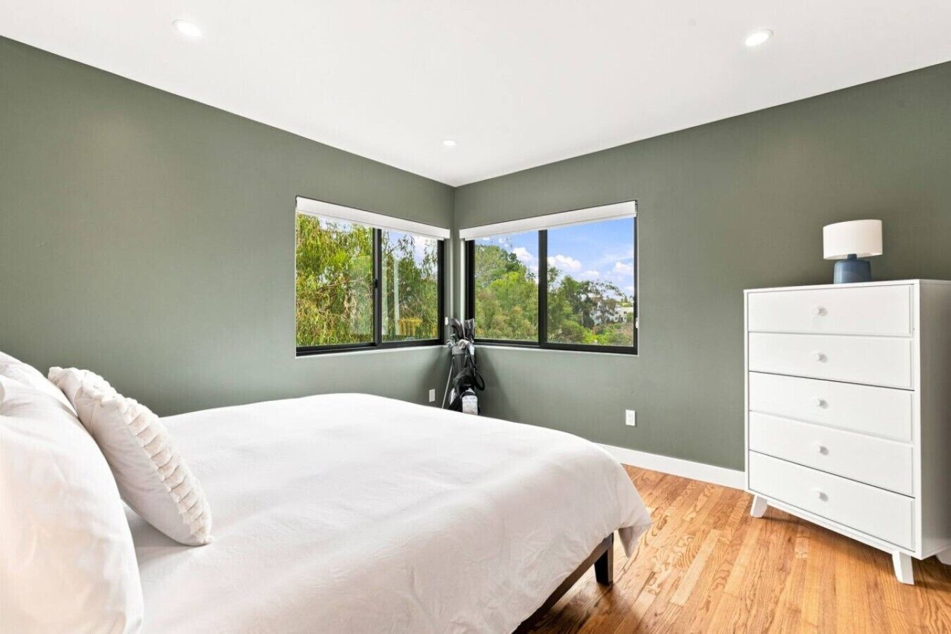 Une chambre à coucher avec un lit, une commode et une fenêtre donnant sur des arbres.