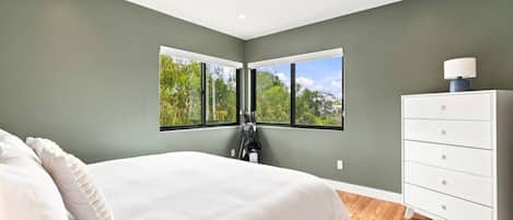 Une chambre à coucher avec un lit, une commode et une fenêtre donnant sur des arbres.
