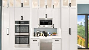 A modern kitchen with white cabinetry, a built-in oven, a microwave, and a coffee maker. - Sunny Palms Luxury Home - Northpark (San Diego)