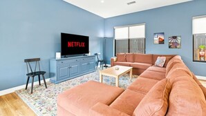 A living room with a sofa, a coffee table, a TV on a cabinet, and a window with a view. - Sunny Palms Luxury Home - Northpark (San Diego)