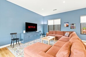 Ein Wohnzimmer mit einer Couch, einem Couchtisch, einem Fernseher auf einem Schrank und einem Fenster mit Blick.