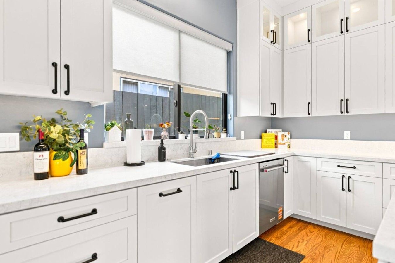 A modern kitchen with white cabinets, a built-in dishwasher, and a window above the sink.