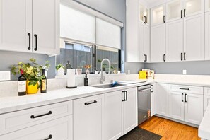A modern kitchen with white cabinets, a built-in dishwasher, and a window above the sink. - Sunny Palms Luxury Home - Northpark (San Diego)